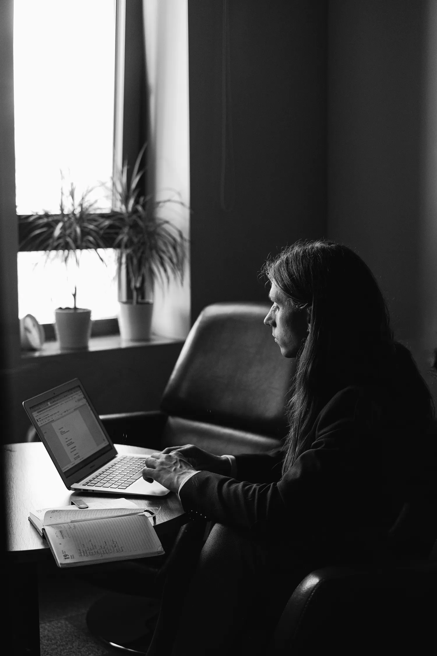 A person works at a laptop with a notebook open beside it.