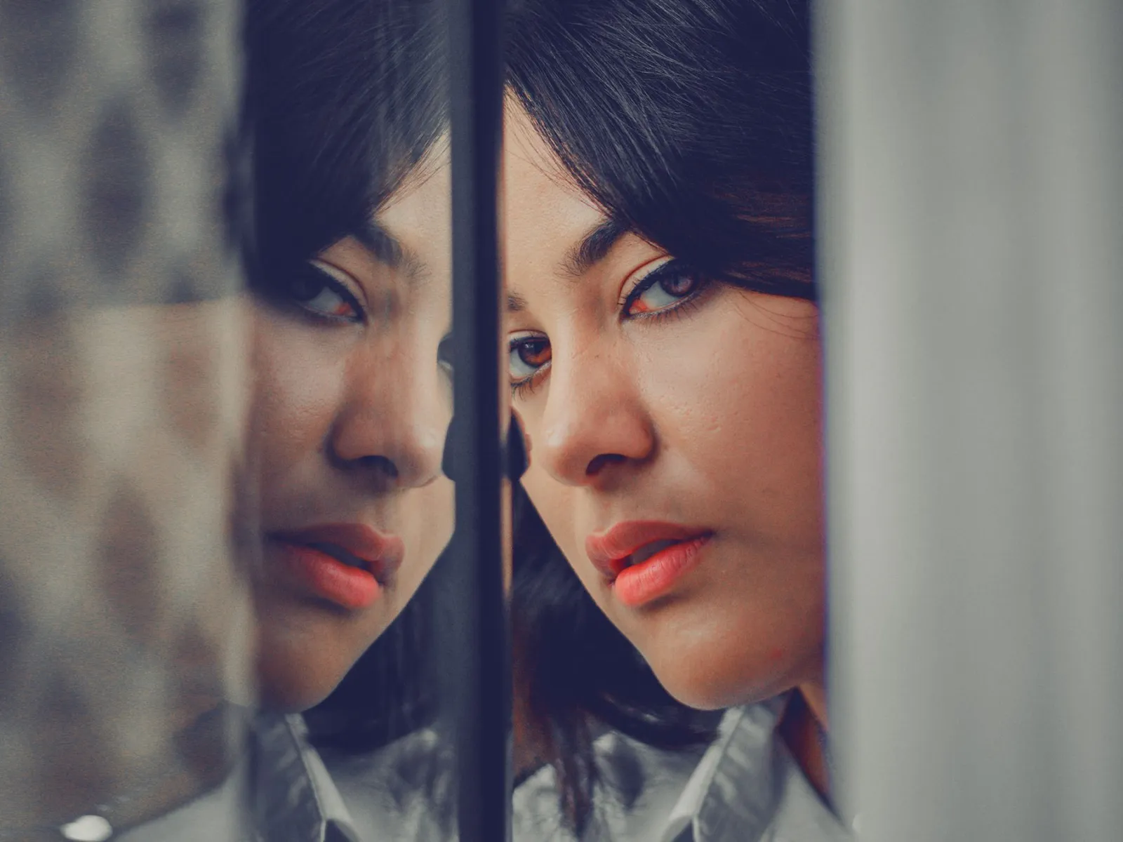 A woman's face and its reflection appear on opposite sides of a window.