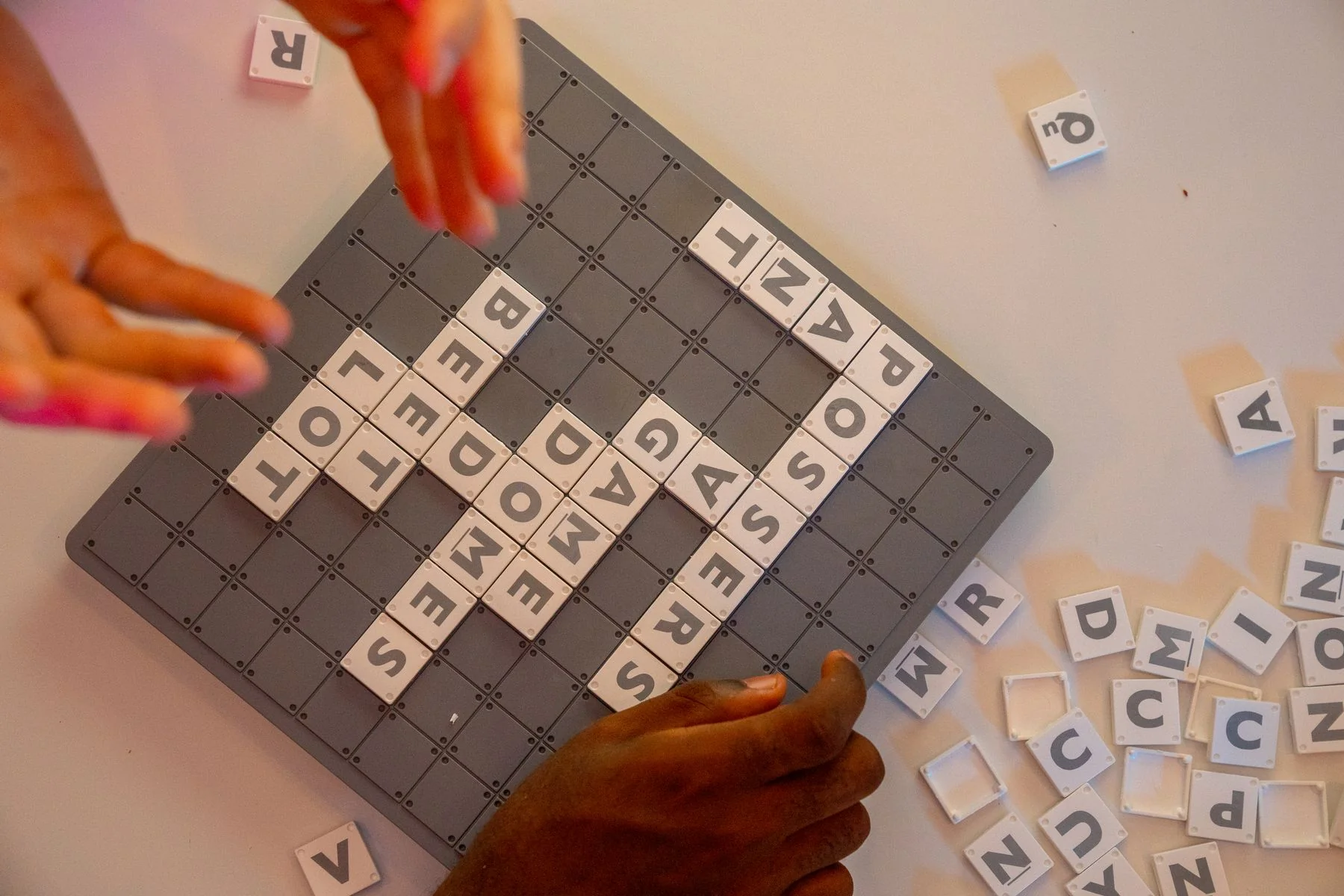 Hands arranging individual letter tiles into words on a board.