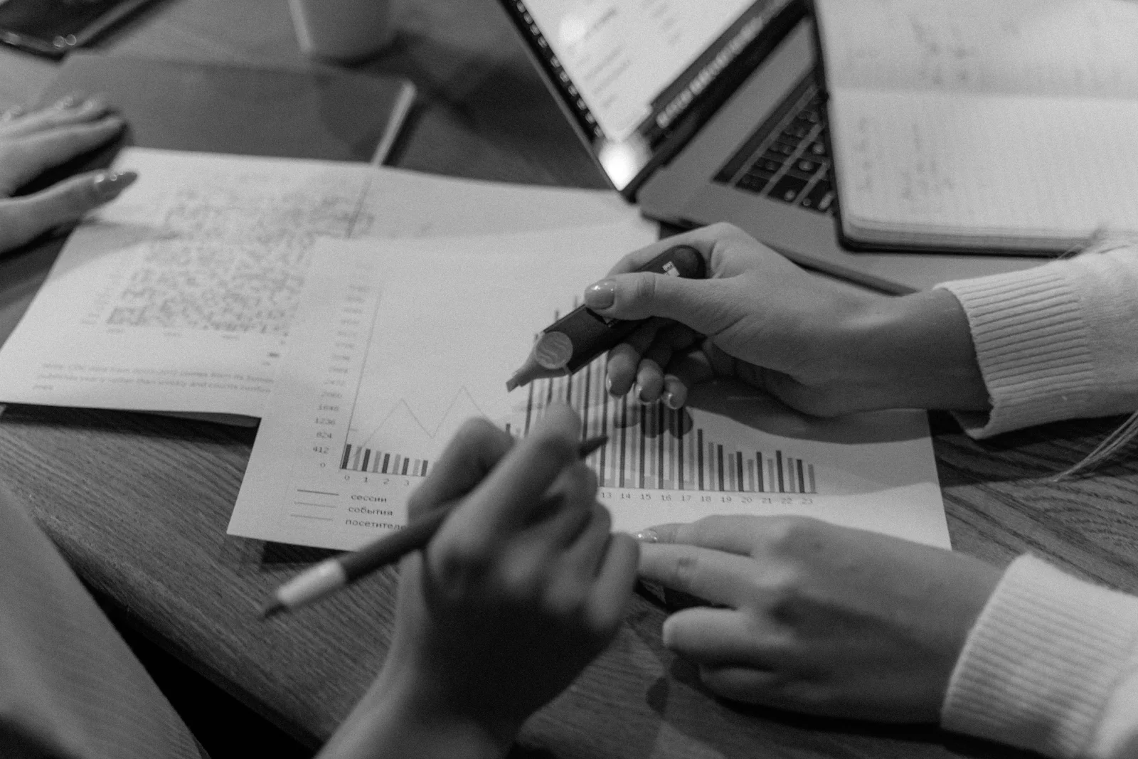 Two people review a printed bar chart beside a laptop and research notes.