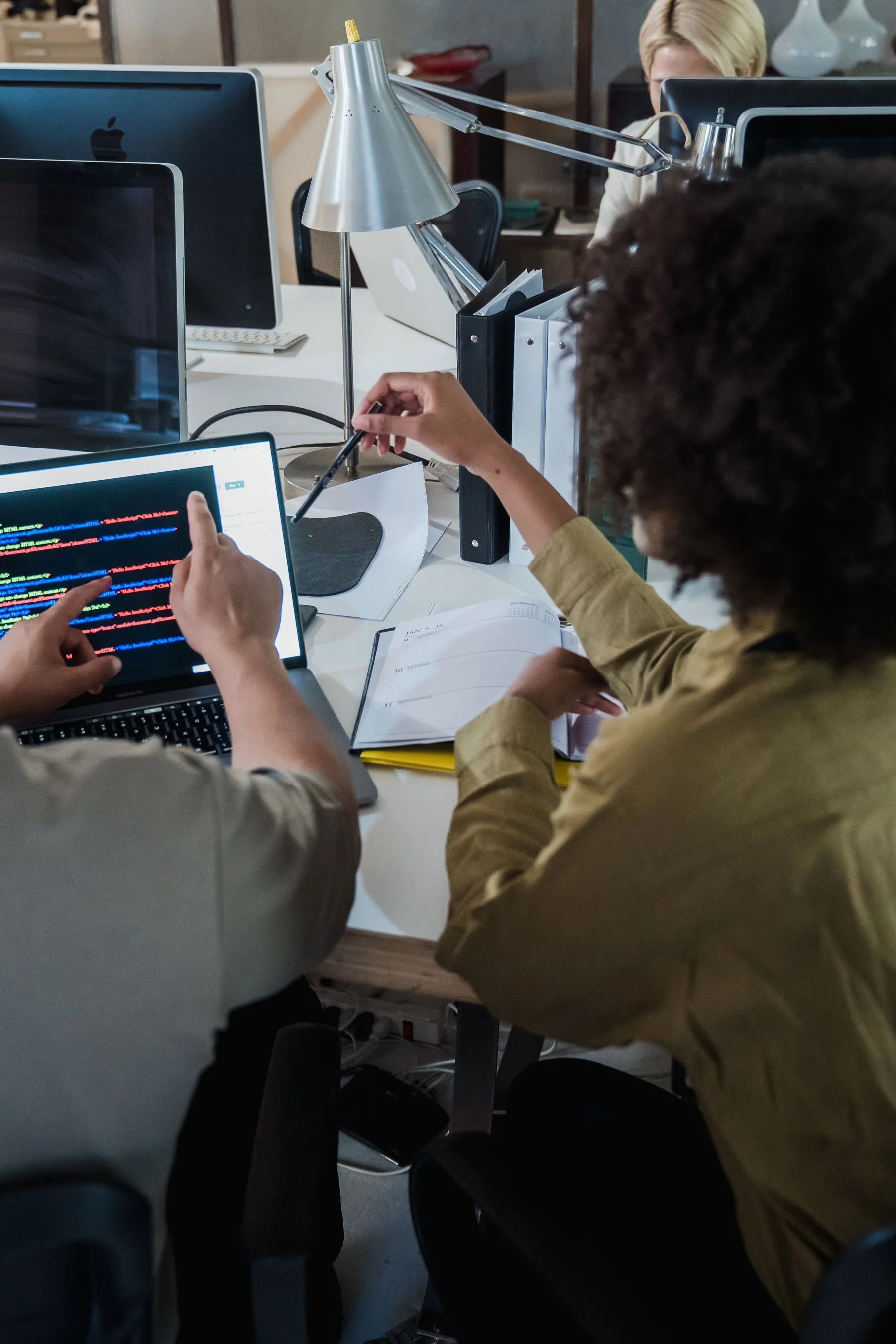 Two colleagues examine code together at a computer.