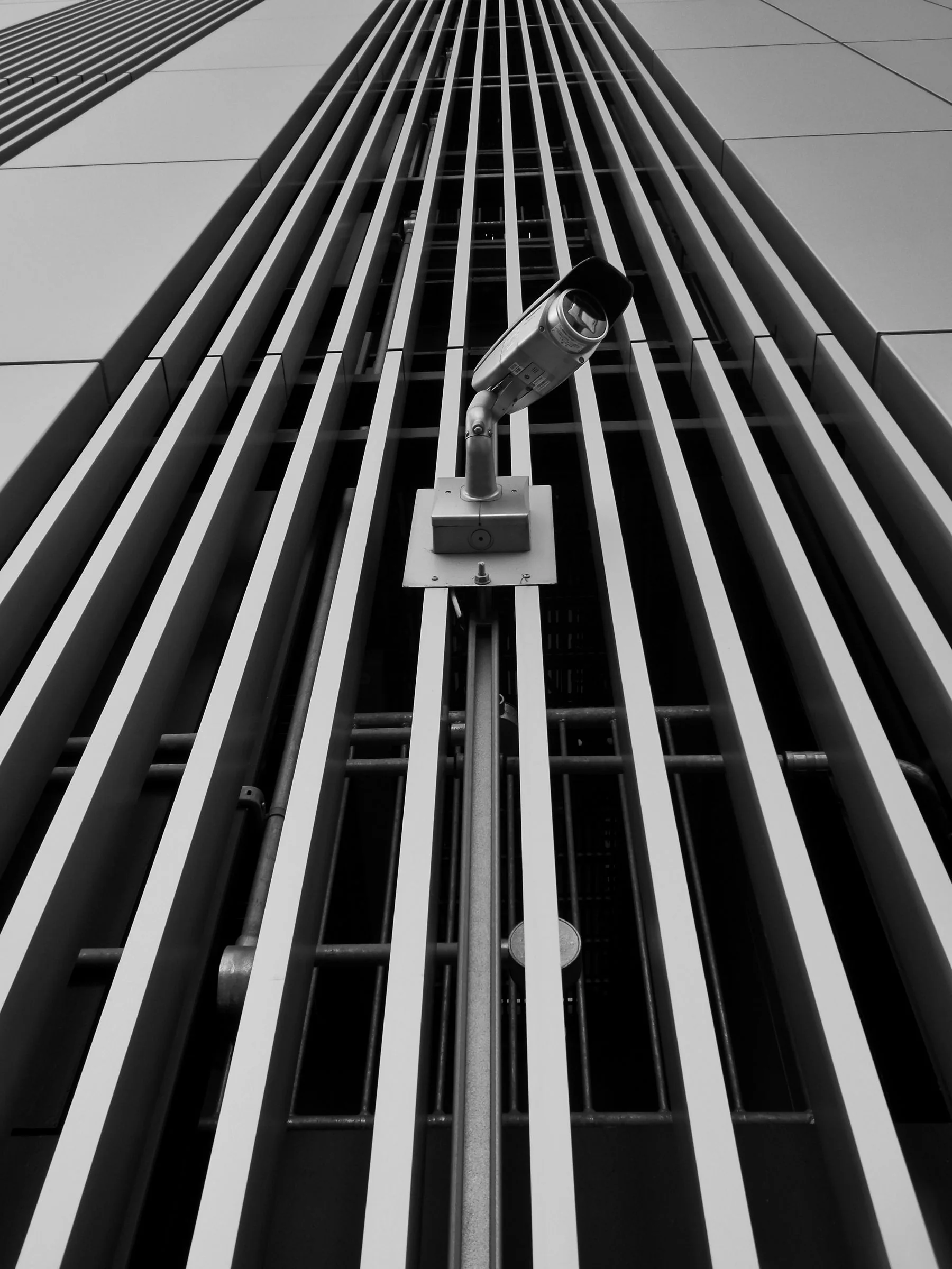 A security camera mounted on a geometric modern building facade.