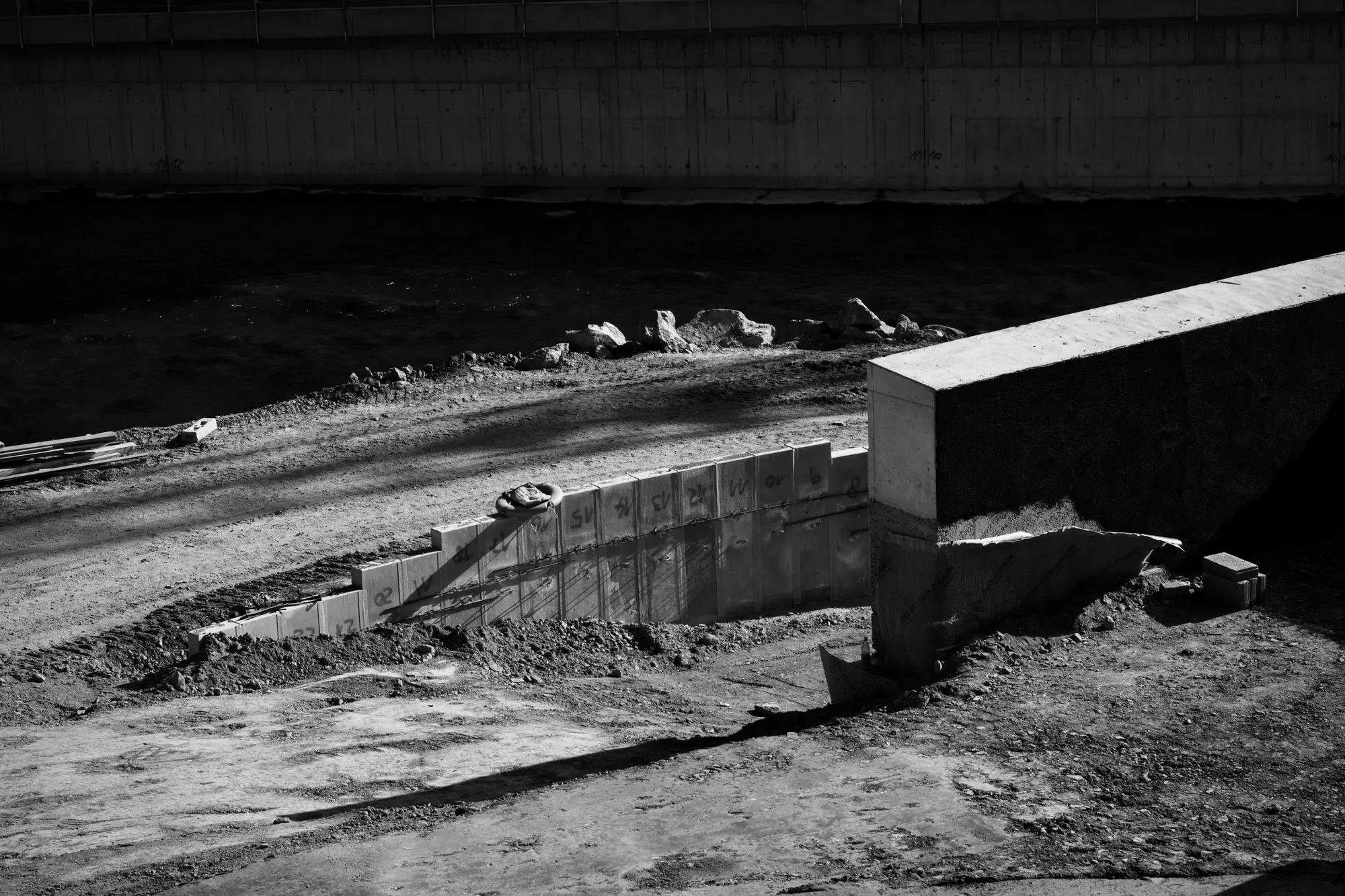 Monochrome construction site with an exposed concrete foundation and retaining wall.