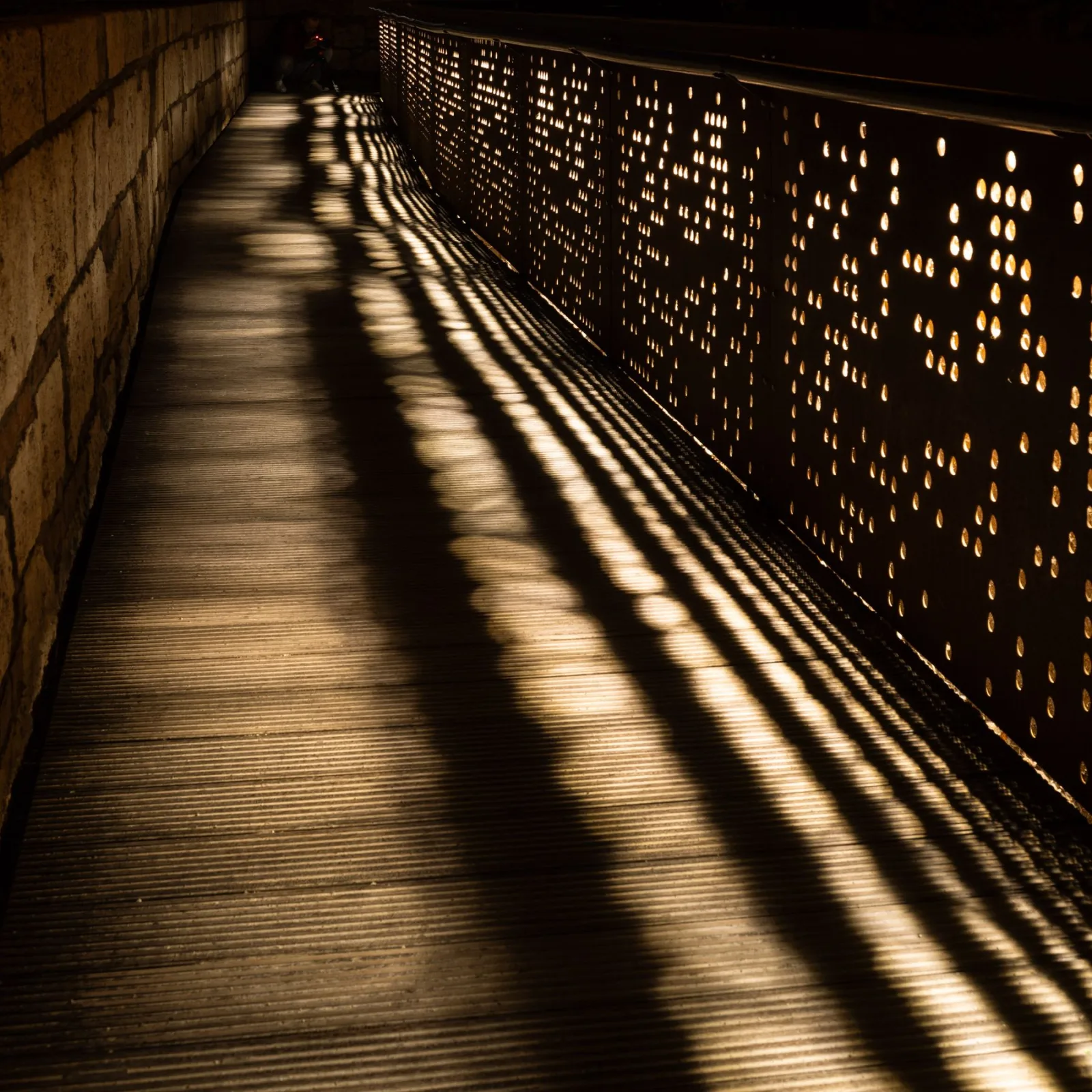 Patterns of light and shadow stretch across a quiet architectural walkway.