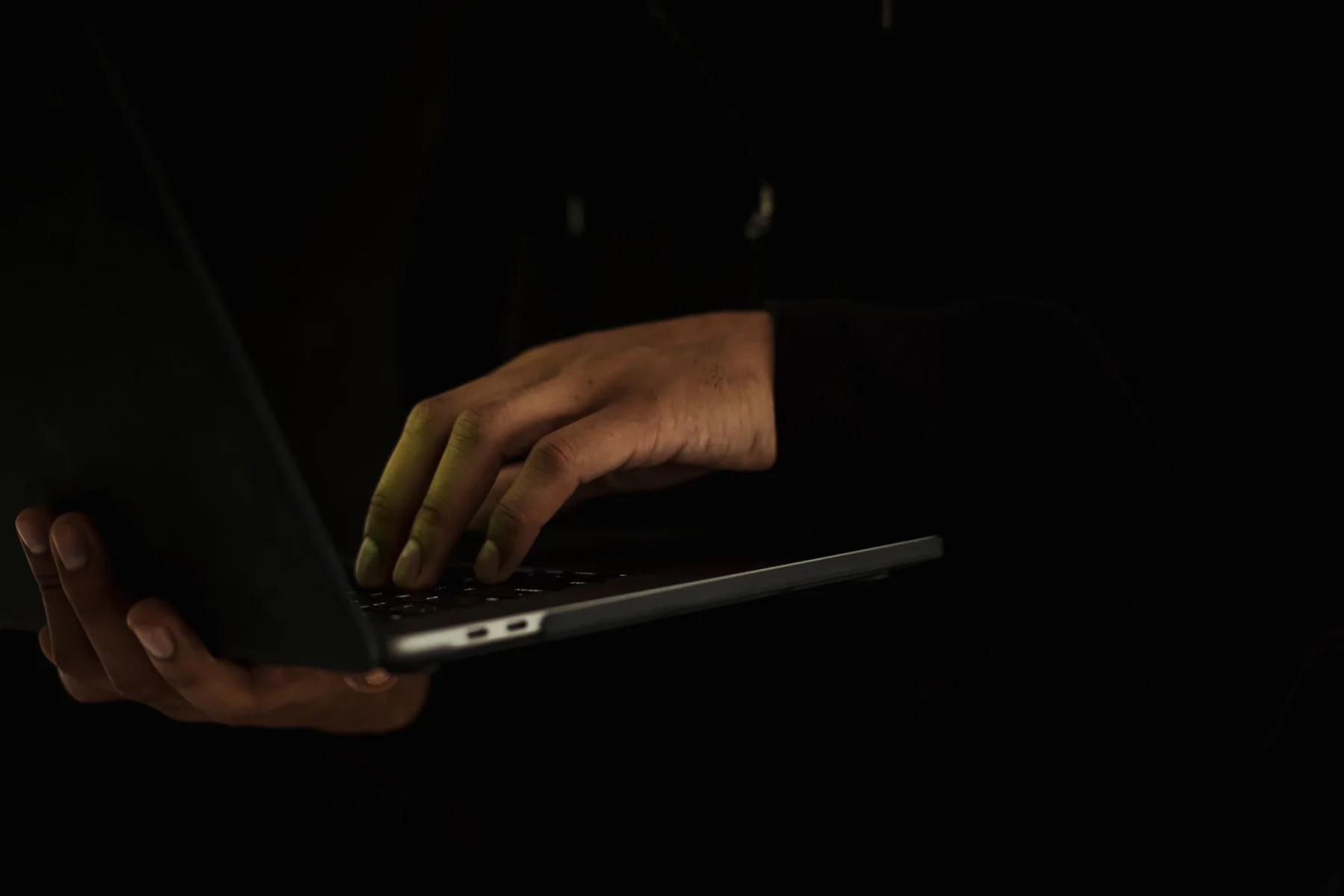 A person uses a laptop in a quiet, dimly lit setting.