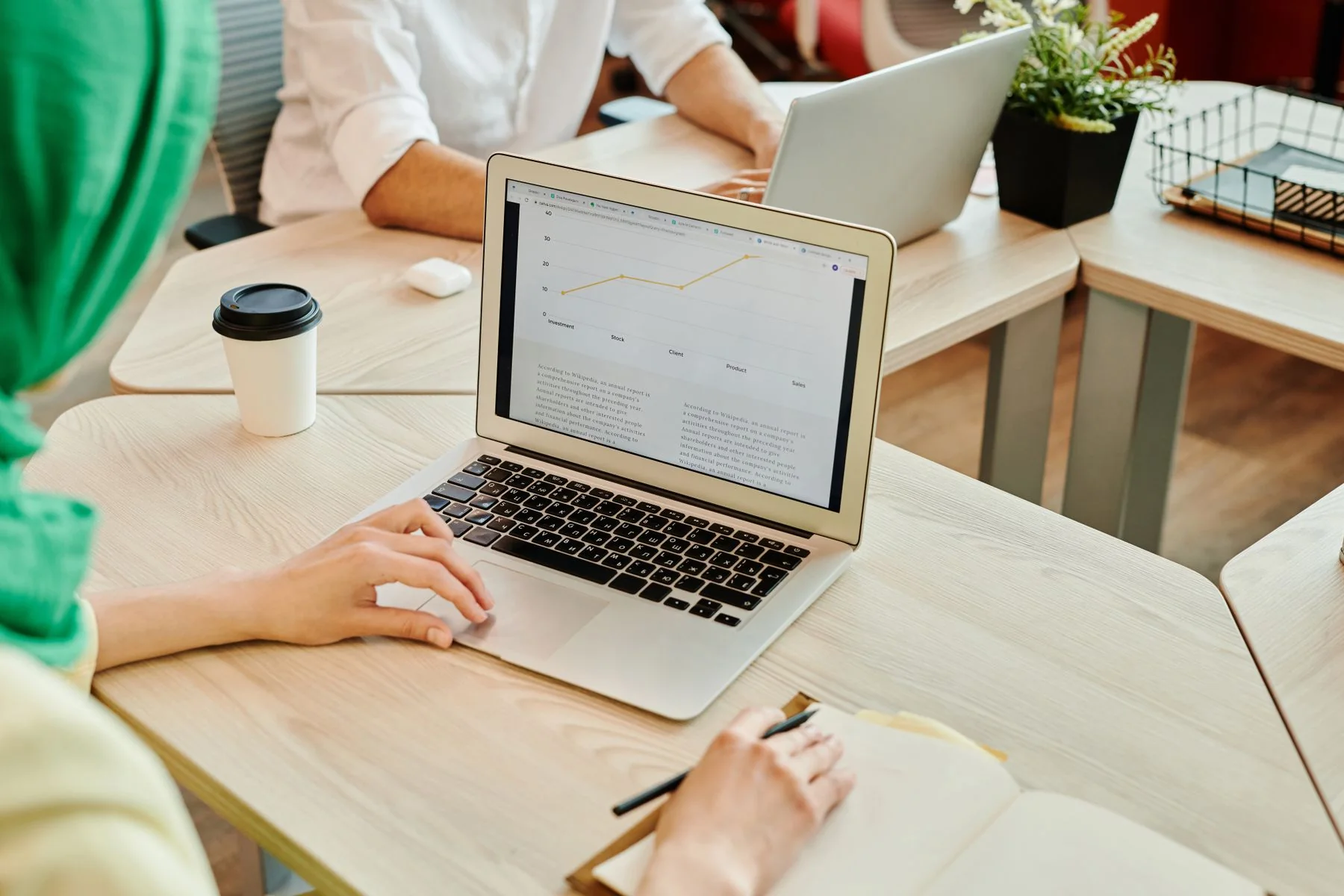 Colleagues work around a laptop displaying a data chart in a bright workspace.