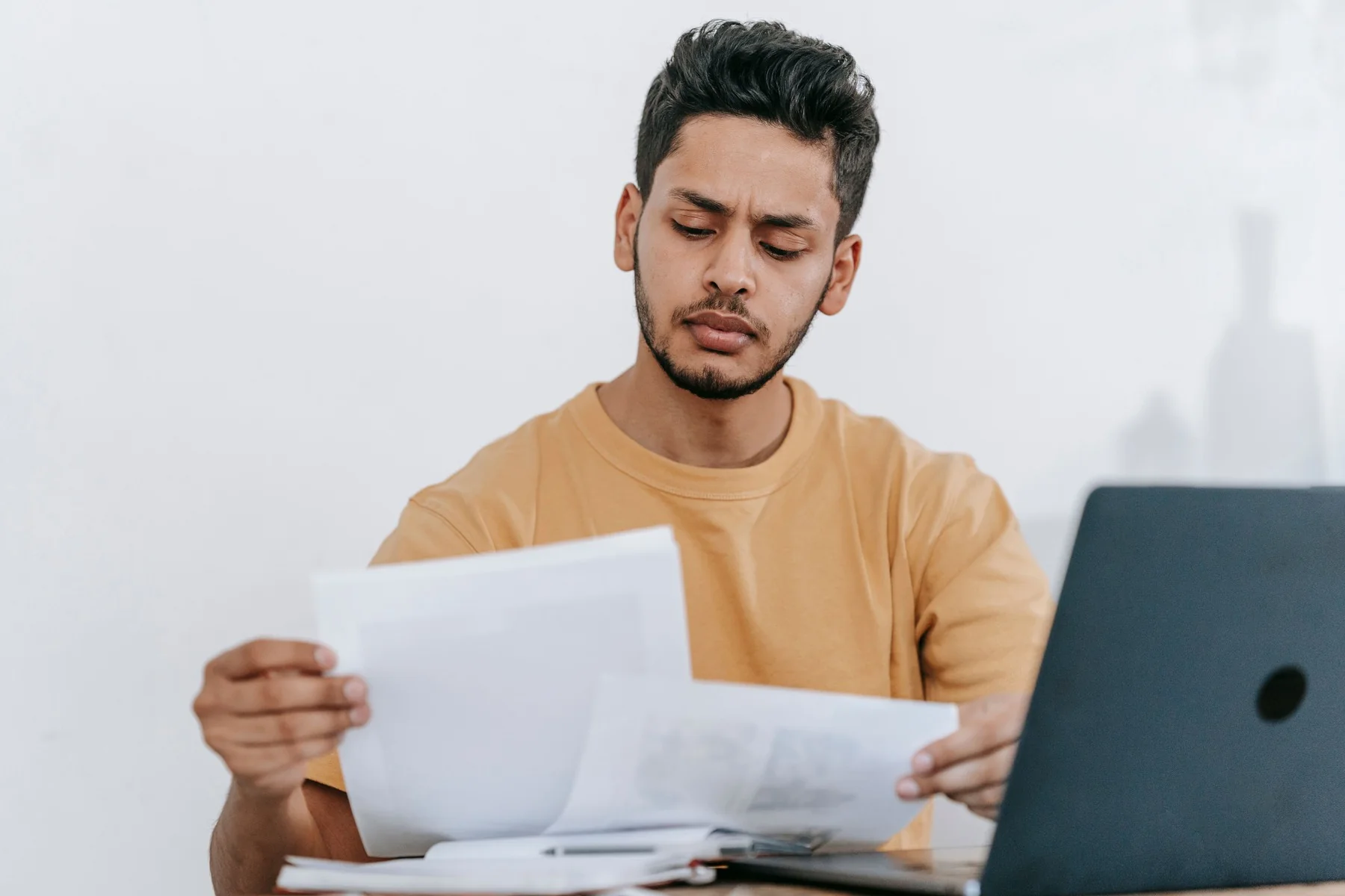 A person reviews printed pages beside an open laptop.