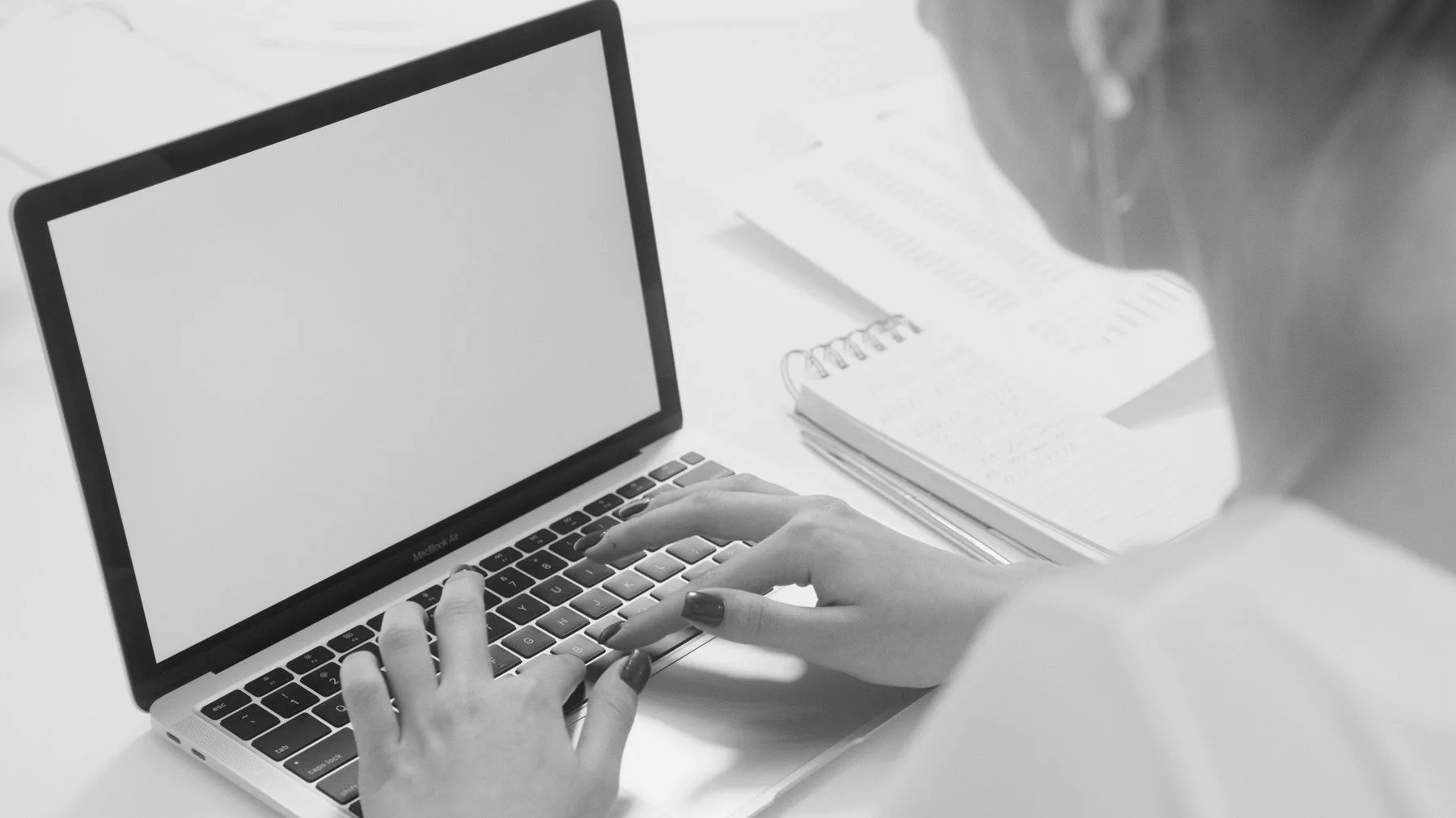 Hands typing at a laptop beside an open notebook.