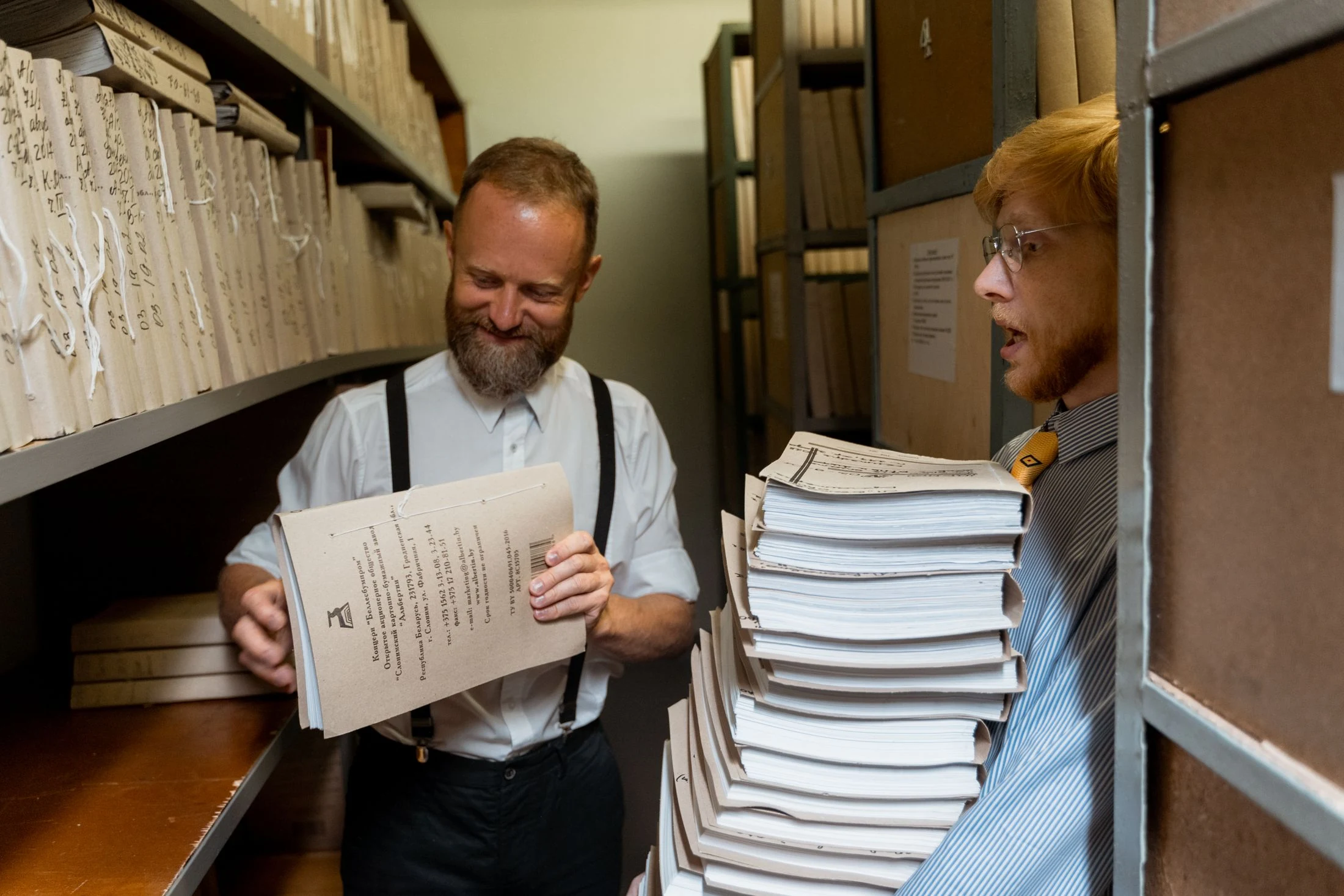 Two archivists sort through folders and paper records in an archive room.