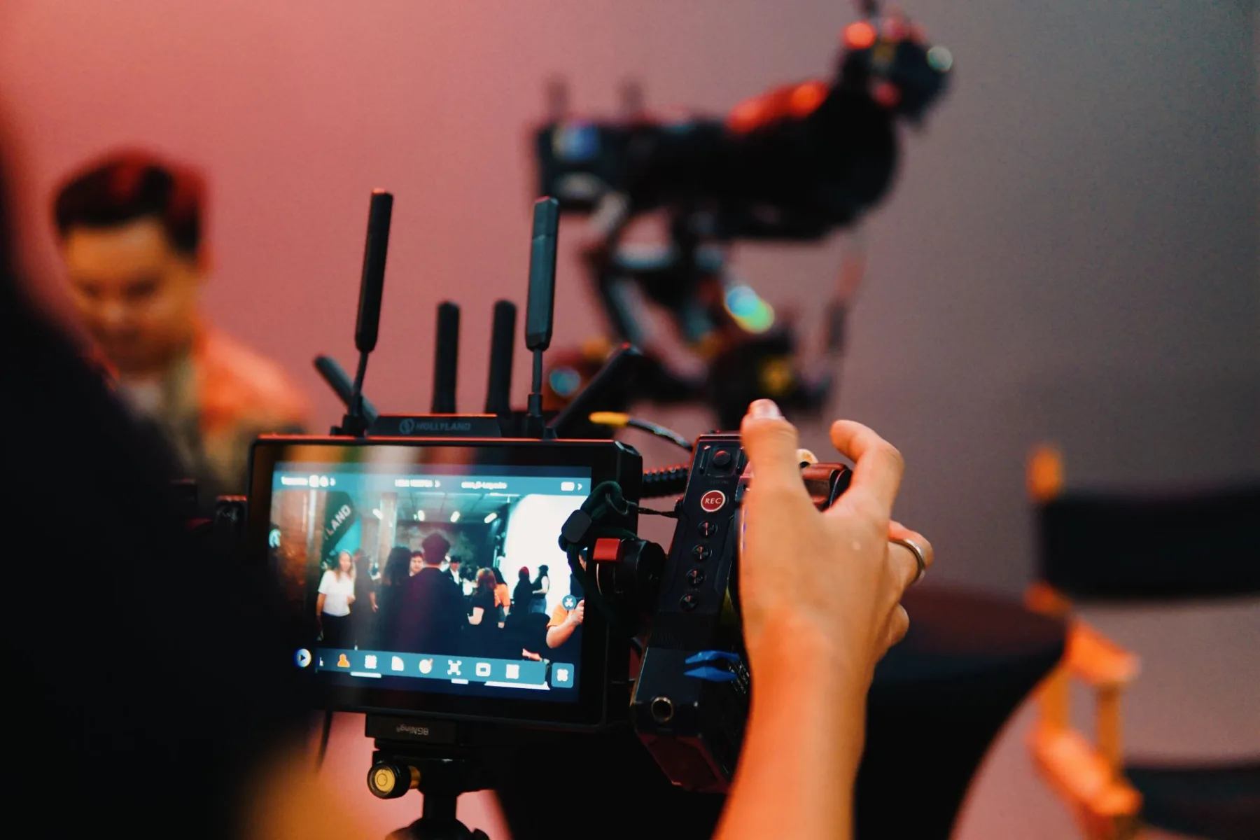 A camera operator films a scene while checking the image on a mounted monitor.